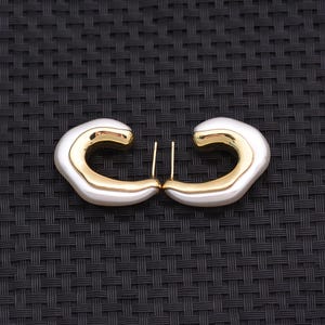 May include: A pair of hoop earrings featuring a two-tone design with a smooth, polished gold-colored inner band and a thick, rounded white outer layer. Each earring has a straight metal post extending from the top for secure attachment.