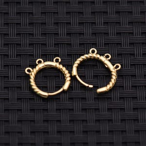 May include: A pair of gold-toned hoop earrings featuring a twisted rope texture. Each circular hoop is designed with three small, evenly spaced loops extending from the outer edge, providing attachment points for additional jewelry components.