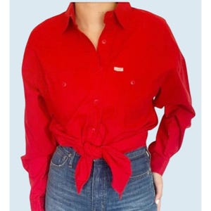 May include: A red long-sleeved button-down shirt tied at the waist. The shirt has a single pocket on the left chest and a small label on the right chest.