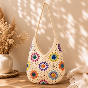 May include: A cream-colored crochet shoulder bag featuring a pattern of multi-colored floral granny squares. The bag has a single integrated strap and a V-shaped opening, constructed from yarn in shades of pink, orange, yellow, blue, and green.