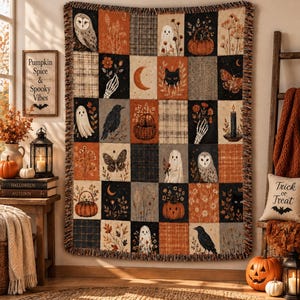 Può includere: Una coperta tessuta con una griglia di pannelli rettangolari con immagini autunnali e di Halloween, tra cui fantasmi, gufi, gatti neri, zucche, corvi, falene, lune crescenti, scheletri e motivi floreali nei toni dell'arancione, nero e crema.