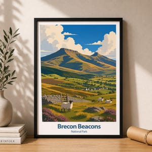 Könnte beinhalten: Ein gerahmter Kunstdruck mit einer Landschaftsillustration des Brecon Beacons Nationalparks. Die Szene zeigt grüne Hügel, ein Gebirge unter blauem Himmel mit weißen Wolken, eine Steinmauer und Schafe. Der Text lautet Brecon Beacons National Park.