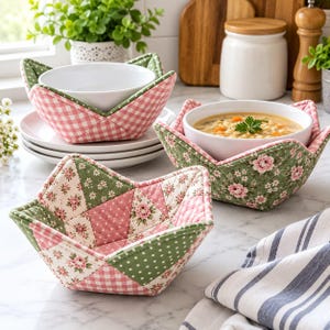 May include: Three fabric bowl cozies featuring quilted patchwork designs in shades of sage green and soft pink. The patterns include floral prints, polka dots, and gingham checks. Two cozies hold white ceramic bowls, one containing soup.