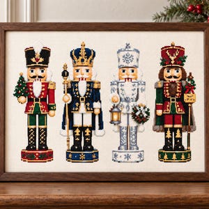 May include: A framed cross-stitch embroidery featuring four distinct nutcracker figures. The figures are dressed in red, blue, white, and green uniforms with detailed gold accents, standing on circular bases, all set against a light fabric background.