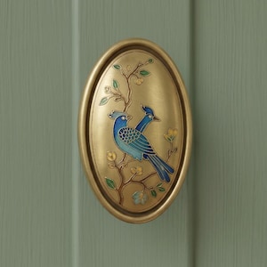 May include: An oval-shaped brass door knocker featuring an inlaid enamel design of two blue birds perched on a flowering branch. The metal has a brushed gold finish, and the birds are depicted with detailed blue feathers and yellow accents.