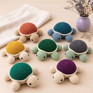 May include: Seven small crocheted turtle toys featuring rounded shells in various colors including rust, teal, yellow, dark green, grey, green, and purple. Each turtle has a cream-colored head, limbs, and a white border around the shell edge.
