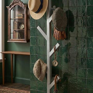 May include: A light gray, tree-shaped wall-mounted coat rack featuring multiple angled branches. The rack holds a straw hat with a navy band, a tweed flat cap, brown leather gloves, a small round compass on a leather strap, and a closed umbrella.