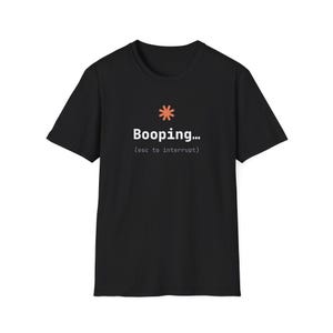 May include: A black short-sleeved t-shirt featuring a coral-coloured asterisk icon above the white text "Booping..." and the smaller grey text "(esc to interrupt)" centred on the chest. The garment has a crew neckline and a standard fit.