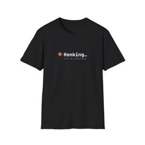 May include: A black short-sleeved t-shirt featuring a graphic on the chest. The design includes an orange asterisk followed by the white text "Honking..." and the smaller white text "(esc to interrupt)" positioned directly underneath.