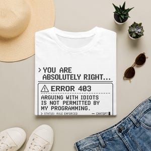 May include: A white t-shirt featuring black pixelated text that reads: > YOU ARE ABSOLUTELY RIGHT... ERROR 403 ARGUING WITH IDIOTS IS NOT PERMITTED BY MY PROGRAMMING. > STATUS: RULE ENFORCED - CHATGPT. The design mimics a computer system error message.