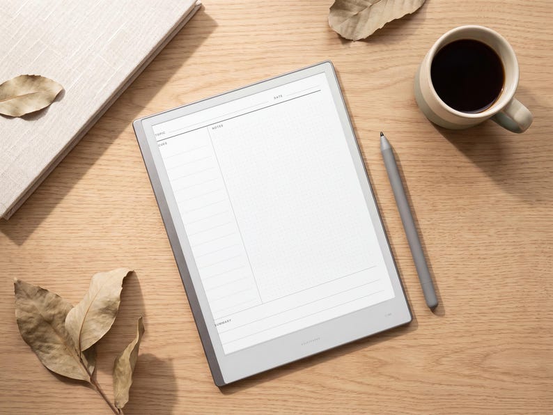 May include: A digital tablet with a light gray frame displaying a white note-taking template with sections labeled Date, Notes, and Summary. A matching gray stylus rests beside the tablet on a wooden surface next to a coffee mug and a notebook.