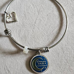 May include: A silver bangle bracelet with a charm that says "I love you to the moon & back" with a crescent moon and stars design. The charm is attached to the bracelet with a silver ring. There is also a small heart charm attached to the bracelet.