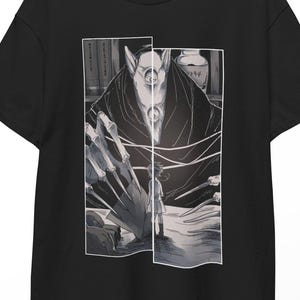 Könnte beinhalten: Ein schwarzes Kurzarm-T-Shirt mit einem rechteckigen Grafikdruck auf der Brust. Die Illustration zeigt eine dunkle, mehräugige Kreatur mit langen, scharfen Krallen, die über einer kleinen Figur in einer monochromen Manga-Stil-Komposition thront.