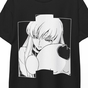 Könnte beinhalten: Ein schwarzes Kurzarm-T-Shirt mit einem zentrierten weißen Grafikdruck. Das Design zeigt eine Manga-Figur mit langem Haar, die sich an eine runde, plüschartige Figur mit einem kleinen dunklen Akzent auf dem Kopf lehnt, eingerahmt in einem Rechteck.