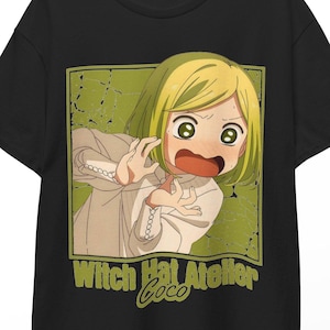 Può includere: Una t-shirt nera a maniche corte con una grafica quadrata di un personaggio anime biondo con un'espressione sorpresa. Il personaggio indossa un indumento chiaro. Sotto la grafica, il testo recita Witch Hat Atelier Coco in verde.