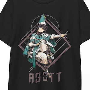 Può includere: Una t-shirt nera a maniche corte con una stampa grafica di un personaggio che indossa un cappello a punta e un mantello color verde acqua, seduto all'interno di una cornice a forma di diamante. Il personaggio tiene un oggetto bianco e il testo AGOTT è stampato in marrone chiaro.