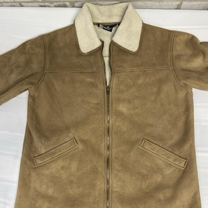 May include: A tan jacket with a cream-colored faux shearling collar and interior lining. The jacket features a full-length front zipper closure, long sleeves, and two slanted welt pockets on the front. The exterior has a smooth, suede-like texture.