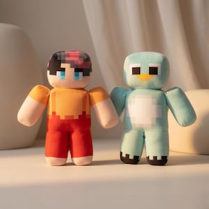 May include: Two plush dolls with blocky, pixelated designs. The left doll has dark hair, blue eyes, an orange shirt, and red pants. The right doll is light blue with a white chest patch, black eyes, and a yellow beak-like feature on its face.
