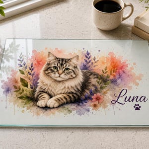 May include: A rectangular glass cutting board featuring a watercolor illustration of a brown tabby cat surrounded by colorful floral accents. The name Luna is printed in a dark purple script font next to a small purple paw print icon on the surface.