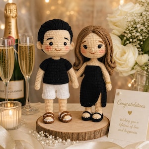 Puede incluir: Dos muñecos amigurumi de pie sobre una rodaja de madera. Un muñeco tiene el pelo negro corto, camiseta negra, pantalones cortos blancos y sandalias marrones. El otro tiene el pelo castaño largo y ondulado, vestido negro con abertura y sandalias negras.