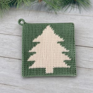 Könnte beinhalten: Ein quadratischer Topflappen aus gehäkeltem, dunkelwaldgrünem Garn mit einem mittig platzierten, cremefarbenen Tannenbaummotiv. Der Topflappen verfügt über eine kleine, runde Schlaufe an der oberen linken Ecke zum Aufhängen und ein dichtes Maschenbild.