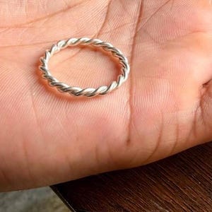 Peut inclure: Une bague de couleur argentée présentant un motif torsadé semblable à une corde. L'anneau est constitué d'un brin métallique continu qui s'enroule sur toute la circonférence, créant un aspect texturé et uniforme sur tout le bijou circulaire.
