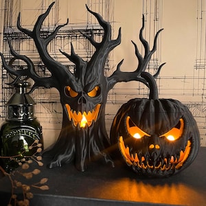 May include: A black 3D printed haunted tree sculpture and a matching black pumpkin jack-o'-lantern, both featuring jagged, menacing facial expressions with glowing orange interior lights that illuminate the eyes and mouths from within.