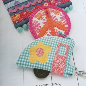 Op de afbeelding: Een verzameling kleurrijke ritszakjes met een retro thema. De ontwerpen omvatten een rechthoekig zakje met denim accenten, een vredesteken en een campervorm, allemaal met heldere kleuren en bloemmotieven. De tekst "HIPPIE ZIPS" is zichtbaar.