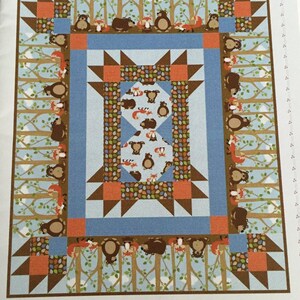 May include: A quilt pattern for a crib quilt featuring a woodland theme with bears and foxes. The pattern is called "Playing In the Woods Crib Quilt" and is designed by Barb Sackel. The fabrics shown are "Into the Woods Flannel" by Northcott Studio.