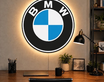 May include: A circular wall-mounted sign featuring the BMW logo with a black outer ring, white lettering, and a blue and white quadrant center. The sign is illuminated from behind with a warm glow, creating a halo effect against the wall.