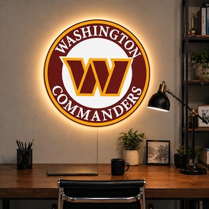 Pode incluir: Um letreiro circular de parede com o logótipo dos Washington Commanders, apresentando um grande W bordô no centro, rodeado por anéis brancos e bordô com o texto WASHINGTON COMMANDERS, iluminado por um efeito de luz de fundo quente.