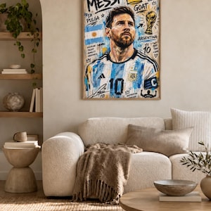May include: A framed vertical wall art print featuring a portrait of Lionel Messi wearing an Argentina soccer jersey. The artwork includes graffiti-style text such as MESSI, GOAT, LA PULGA, and ARGENTINA, along with a gold trophy illustration.