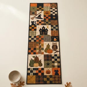 Könnte beinhalten: Ein rechteckiger, gesteppter Tischläufer mit einem Patchwork-Design aus orangefarbenen, schwarzen und grünen Karomustern. Die Applikationen zeigen ein Spukhaus, schwarze Katzen, Kürbisse, eine Eule, einen Hexenhut, einen Besen und Zuckermais.