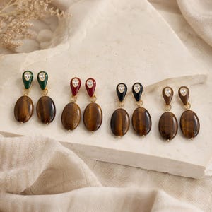 Peut inclure: Quatre paires de boucles d'oreilles pendantes composées de pierres œil-de-tigre ovales suspendues à des clous en forme de goutte. Les clous sont ornés de petits cristaux clairs et se déclinent en vert foncé, rouge profond, noir et marron.