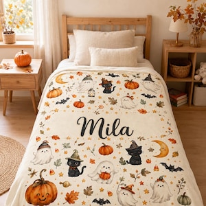 Peut inclure: Une couverture en polaire crème avec un motif répétitif d'Halloween composé de fantômes, de chats noirs avec des chapeaux de sorcière, de citrouilles, de chauves-souris et de croissants de lune. Le prénom Mila est écrit en lettres cursives noires.