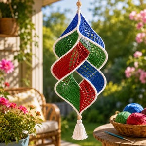 May include: A hanging spiral decoration crafted from crocheted yarn in vibrant blue, green, and red segments, each outlined with white trim. The structure features a central wooden bead at the top and bottom, with a white tassel hanging below.