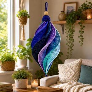 May include: A hanging crochet ornament featuring a spiraling, twisted shape with a gradient color scheme transitioning from deep navy blue and purple at the top to lighter shades of teal and aqua at the bottom, finished with a wooden bead.