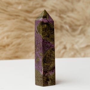 May include: A polished crystal tower featuring a hexagonal prism shape with a pointed top. The stone displays a mottled pattern of deep olive green and vibrant purple mineral inclusions, with visible natural veining throughout the surface.