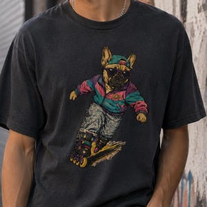May include: A charcoal grey short-sleeve t-shirt featuring a graphic print of a French bulldog wearing sunglasses, a teal and magenta windbreaker, and a baseball cap while rollerblading on a yellow surface with a dark, textured appearance.