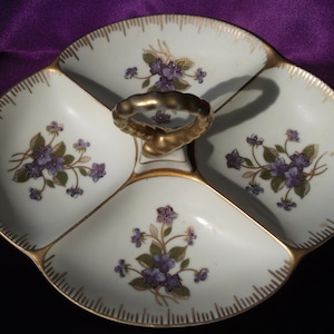 May include: A white porcelain serving dish with a gold trim and floral design. The dish is divided into four sections and has a handle in the center.