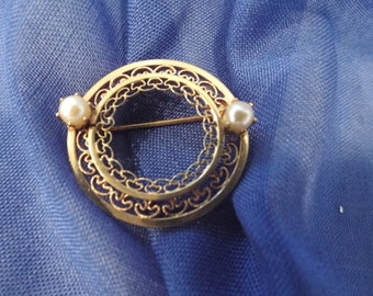 May include: A gold filigree brooch with two small white pearls. The brooch is in the shape of a circle with a delicate design.