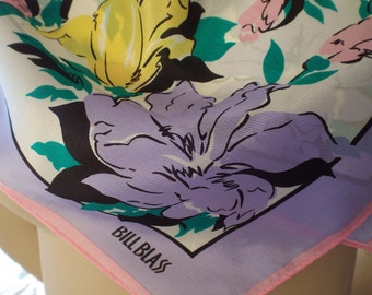 May include: A purple, yellow, and pink floral print silk scarf with a pink border and the text "Bill Blass" in black.