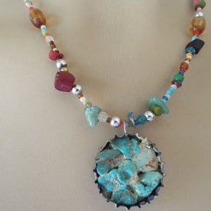 May include: A turquoise and silver necklace with a large turquoise pendant. The necklace is made with a variety of beads, including silver, amber, and red.