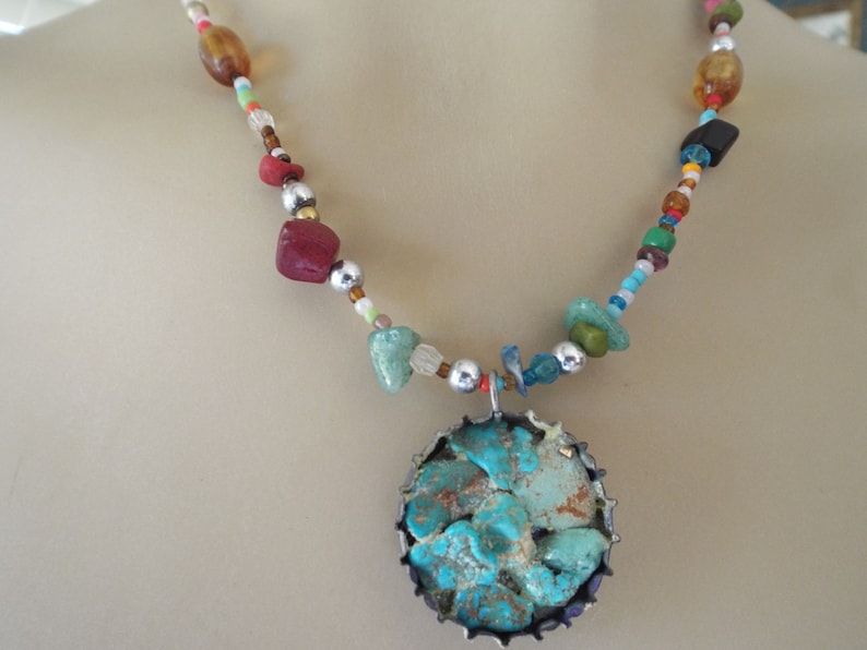 May include: A turquoise and silver necklace with a large turquoise pendant. The necklace is made with a variety of beads, including silver, amber, and red.