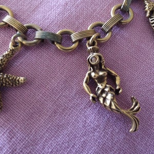 May include: A gold chain bracelet with a mermaid, starfish, and seahorse charms. The charms have small pink gemstones.
