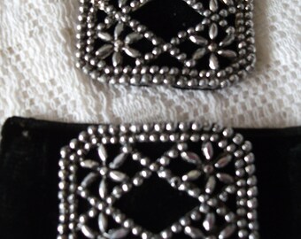 May include: Two black velvet belt buckles with silver metal embellishments. The embellishments are in a geometric pattern of small circles and ovals.