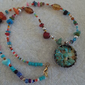 May include: A turquoise and silver necklace with a variety of colorful beads, including red, orange, yellow, green, blue, and purple. The necklace has a large turquoise pendant with a silver setting.