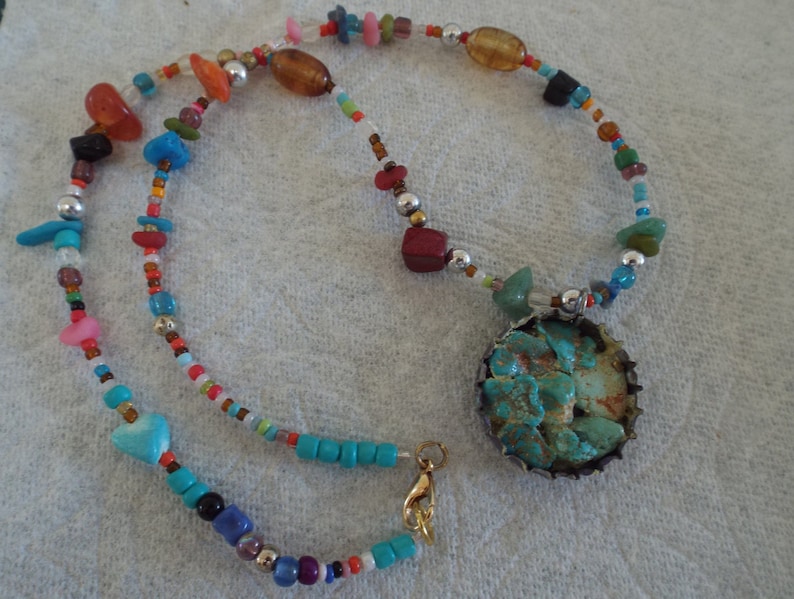 May include: A turquoise and silver necklace with a variety of colorful beads, including red, orange, yellow, green, blue, and purple. The necklace has a large turquoise pendant with a silver setting.