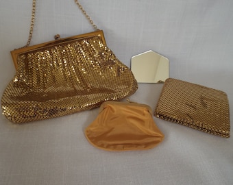 May include: A collection of vintage gold mesh purses and a small mirror. The purses vary in size and shape, including a clutch with a chain strap, a small coin purse, and a rectangular evening bag.
