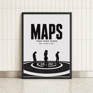 May include: A framed rectangular poster featuring the word MAPS in large black letters, followed by YEAH YEAH YEAHS and 2003 FEVER TO TELL. Three black silhouettes of people stand on a circular black and white target pattern against a white background.